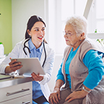 An older, white-haired woman looks at a chart with her doctor, a younger woman.