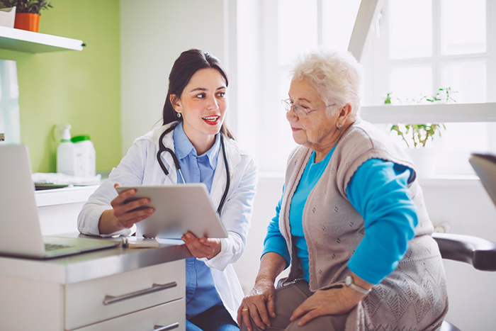 An older, white-haired woman looks at a chart with her doctor, a younger woman.