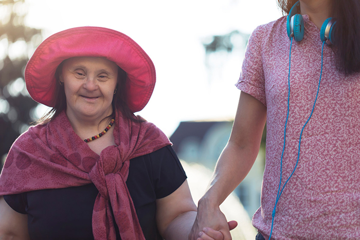 Older woman with Down syndrome, holding the hand of a younger woman.