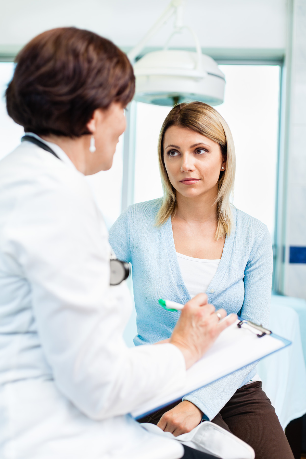 Medical professional with pen and clipboard talking with woman who looks concerned.