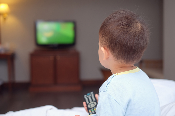 A child holding a television remote control device, facing a television set.