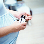 Side view of the torso of a pregnant woman holding a medicine bottle in one hand and pills in the other.