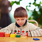 A boy seated at a table, looking at tiles.