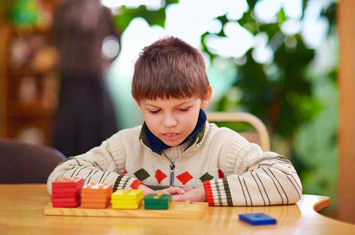 A boy seated at a table, looking at tiles.