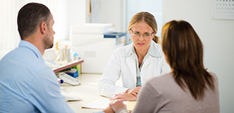 A man and woman talking to a woman in a white lab coat.