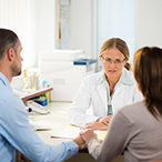 A man and woman talking to a woman in a white lab coat.