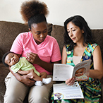 New mom with infant looks over Safe Infant Sleep recommendations with another woman.