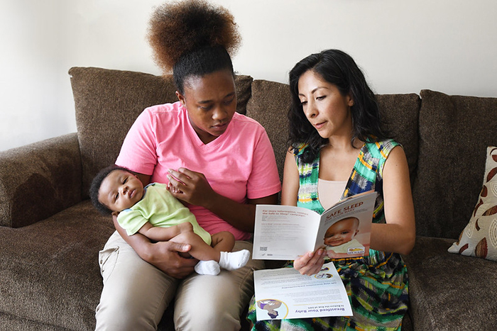 New mom with infant looks over Safe Infant Sleep recommendations with another woman.