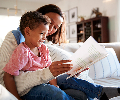 A little boy sits in a woman’s lap, laughing as she reads to him.