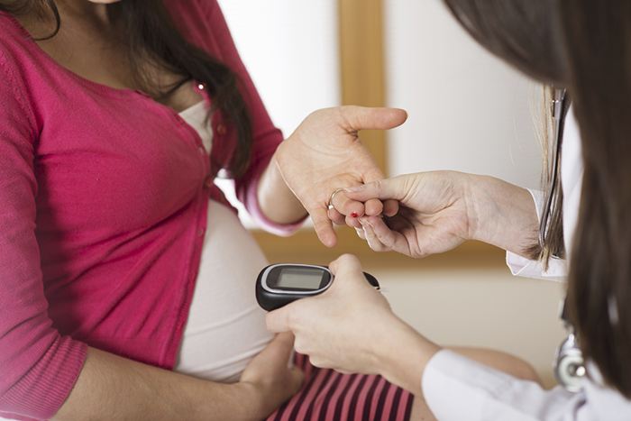 Pregnant woman holding her hand out for a healthcare worker to test her blood sugar test.
