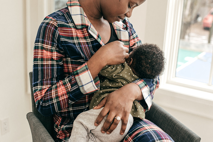 A mother breastfeeds her infant inside their home.