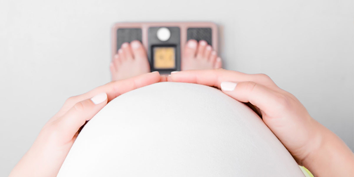 Pregnant woman stands on a scale with her hands on her belly.