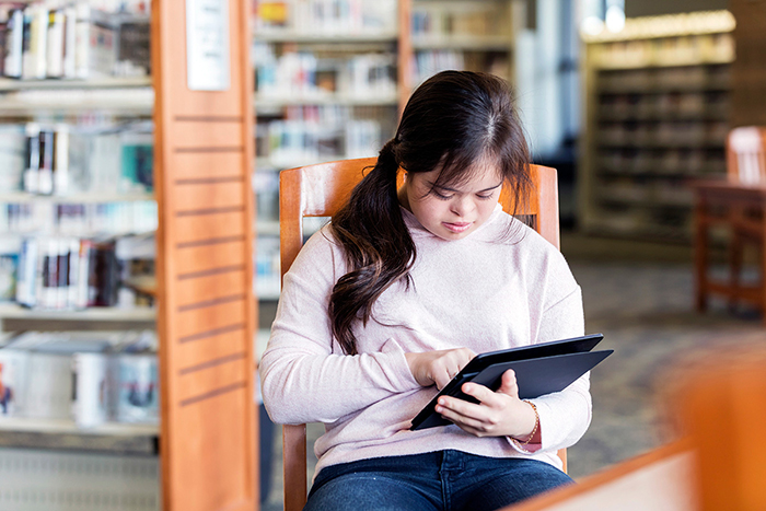 Young woman with Down syndrome typing on a computer tablet.