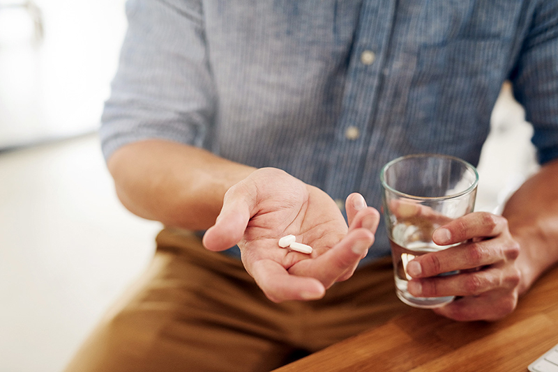 A man holds 2 pills in one hand and a glass of water in his other hand.