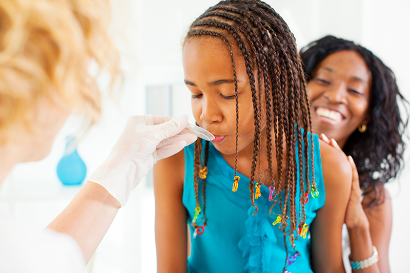 A girl receives medicine from a healthcare provider while her mother looks on.