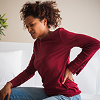 Adolescent woman rubbing back with one hand while grimacing in pain.