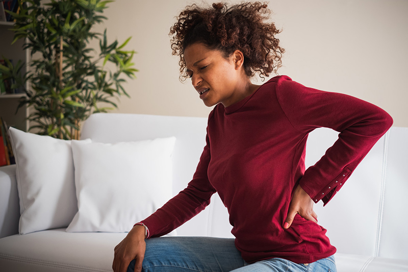 Adolescent woman rubbing back with one hand while grimacing in pain.