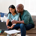 A woman and man participate in a videoconference in their living room.