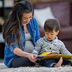 Woman and child sitting on a rug reading a book together.