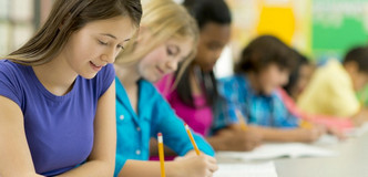 Teen boys and girls, seated at a long table, filling out a form with pencils.
