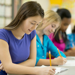 Teen boys and girls, seated at a long table, filling out a form with pencils.