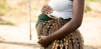 Side view of pregnant woman’s torso, hands on abdomen.