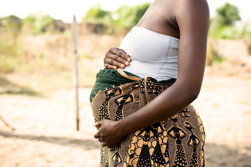 Side view of pregnant woman’s torso, hands on abdomen.