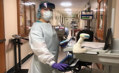 Nurse in protective gear in hospital hallway.