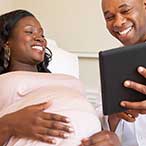 A pregnant woman and her healthcare provider smile at a tablet, which presumbably contains test results or other health information.