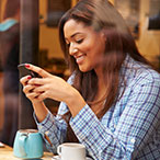 A young woman is smiling while using her cellphone.