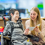 Child in wheel chair and woman reading a pamphlet together.