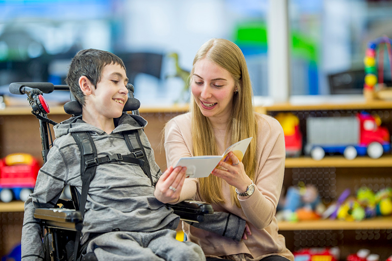 Child in wheel chair and woman reading a pamphlet together.