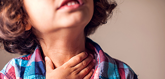 Close up of a child with their hand on their throat.