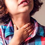 Close up of a child with their hand on their throat.