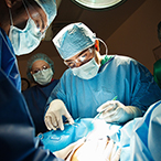 Doctors and nurses in surgical garb standing over a patient’s draped torso.