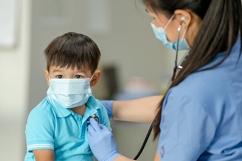 Boy seated while healthcare provider listens to his heart with a stethoscope.