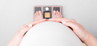Point-of-view image of pregnant woman looking over abdomen at feet on scale.