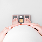 Point-of-view image of pregnant woman looking over abdomen at feet on scale.