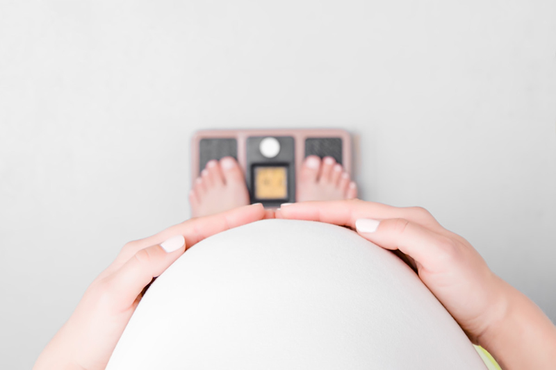 Point-of-view image of pregnant woman looking over abdomen at feet on scale.