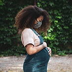 A pregnant woman is outside, wearing a facemask.