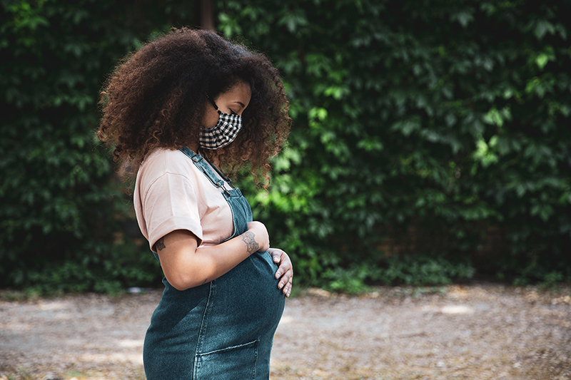 A pregnant woman is outside, wearing a facemask.