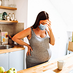 Stressed pregnant woman standing in kitchen.