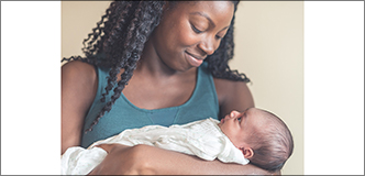 An African American woman smiling at the baby she’s holding in her arms.