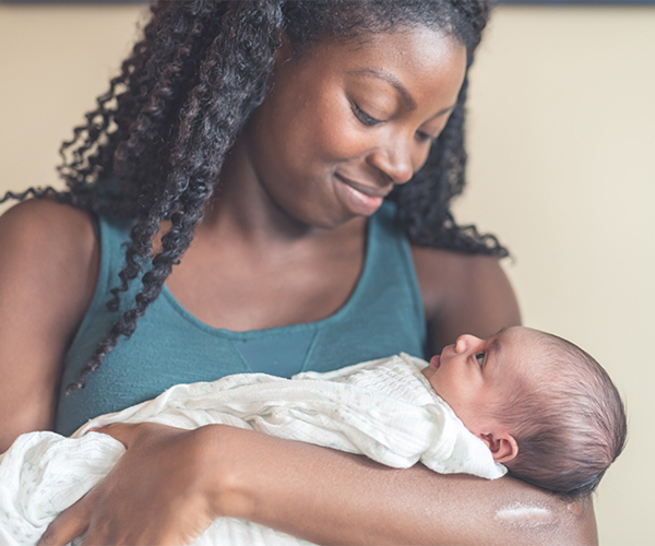 An African American woman smiling at the baby she’s holding in her arms.