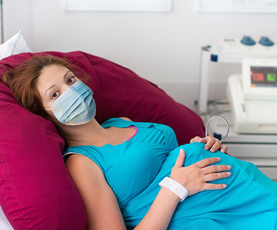 Pregnant woman with a face mask lying on an examination room table.