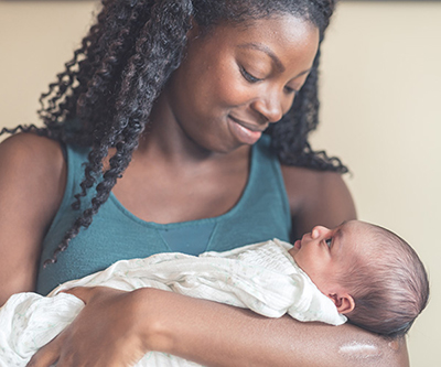 An African American woman smiling at the baby she’s holding in her arms.