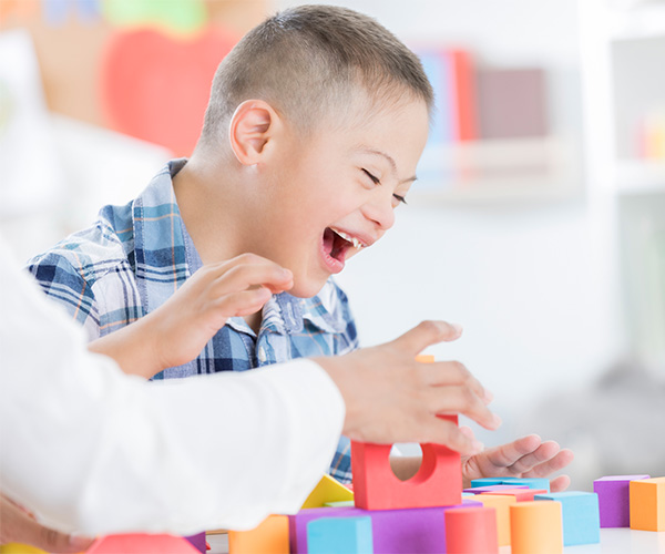 A young boy with Down syndrome laughing as he plays with building blocks.