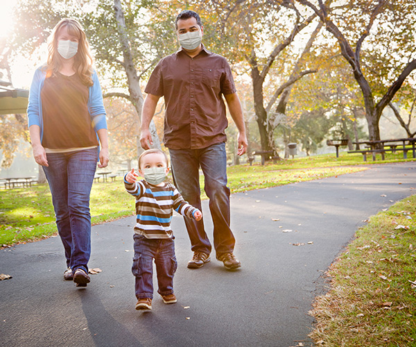 Parents and their infant, all wearing protective face masks, walking outdoors.