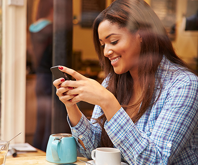 Woman sitting at a café table, checking her mobile device.