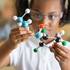 Elementary science student using plastic atom model educational toy.